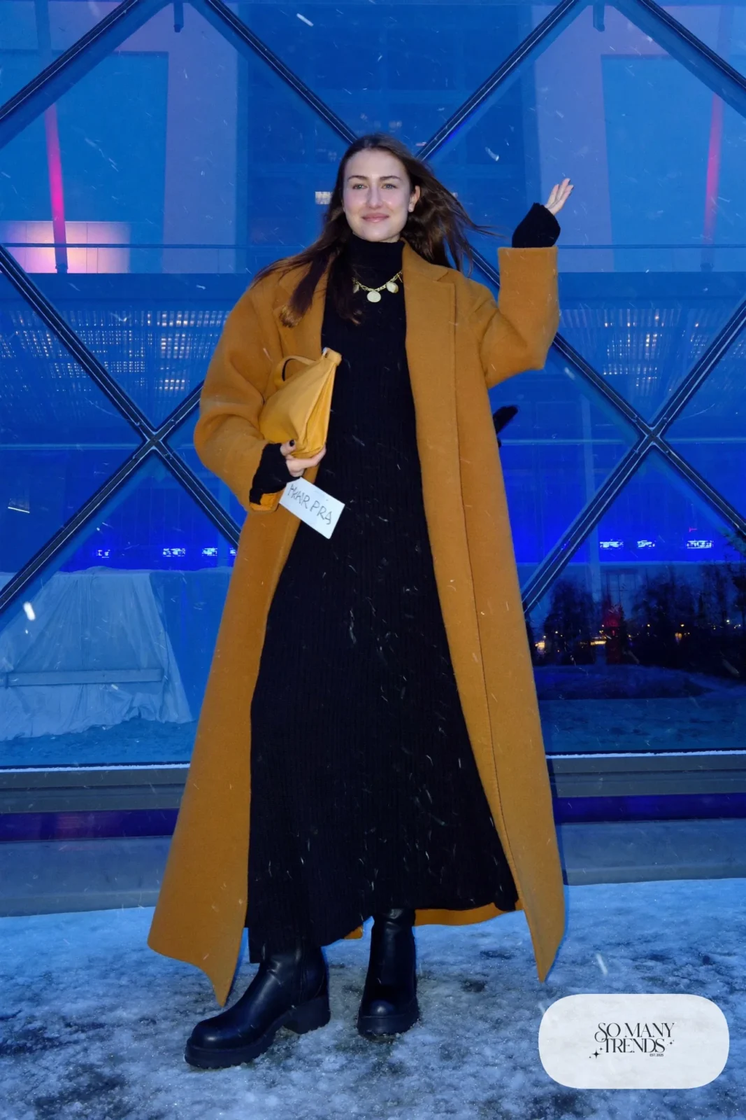Woman in a black knit maxi dress, camel coat, black boots and gold necklace outside Harpa concert hall, outfit 26