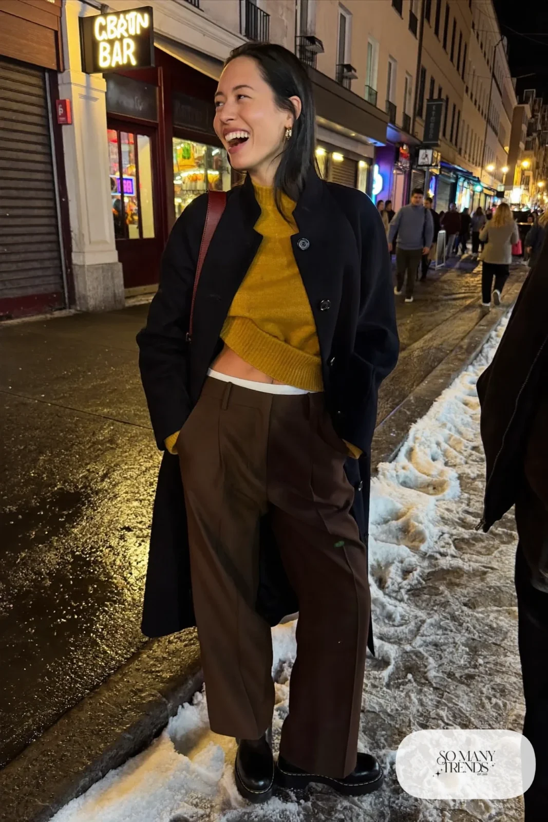 Woman in a black long coat, mustard fine knit, chocolate wide-leg pants and lug boots on a Reykjavik night street, outfit 28