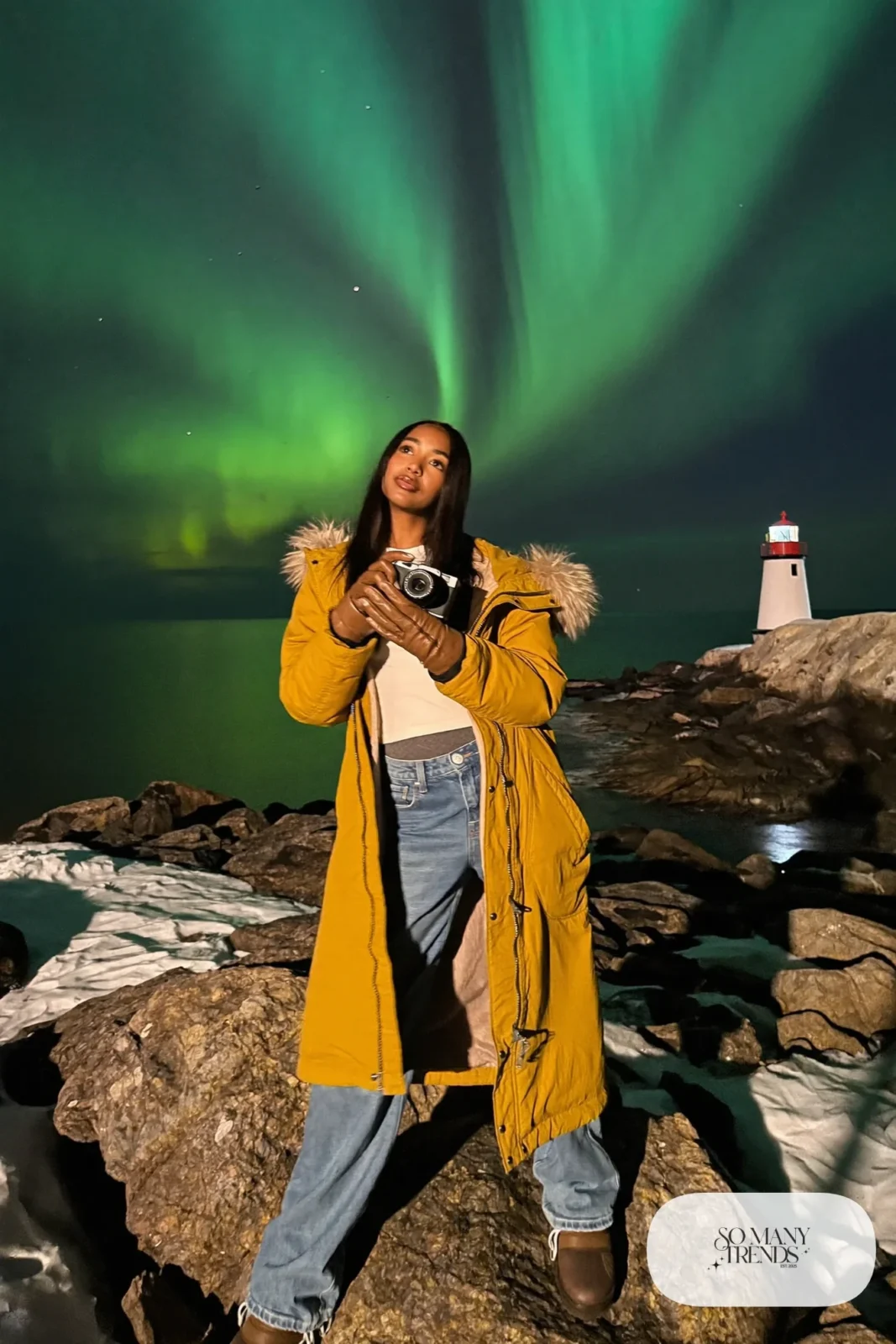 Woman in a mustard parka, denim blue jeans, brown boots and cream beanie by Grotta lighthouse under aurora, outfit 29