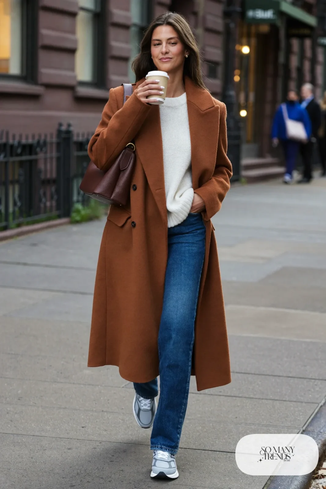 Woman in long terracotta wool coat, cream knit, straight indigo jeans and gray New Balance 9060 sneakers, outfit 1