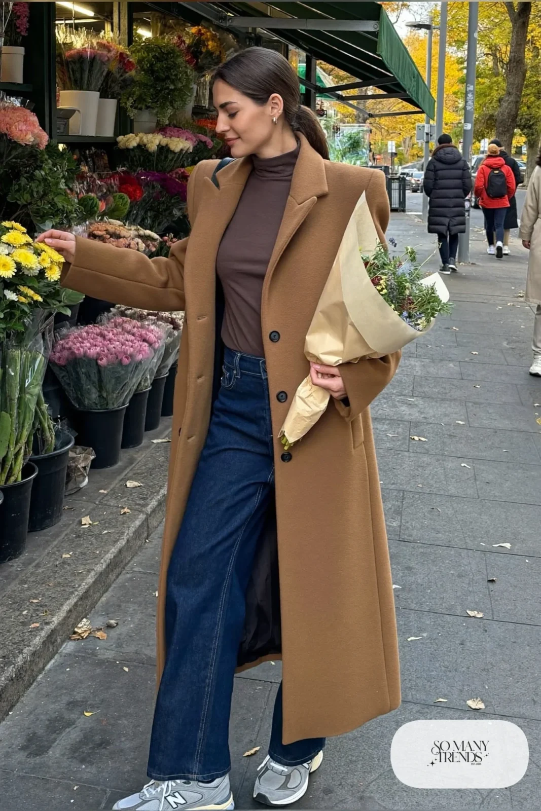 Woman in camel wool coat, chocolate brown turtleneck, barrel-leg jeans and gray New Balance 9060 sneakers, outfit 4