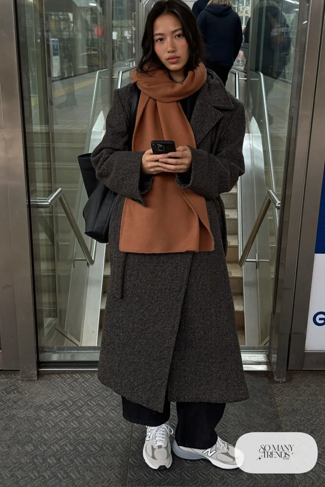 Woman in charcoal herringbone coat, terracotta scarf, black wide-leg pants and gray New Balance 9060 sneakers, outfit 5