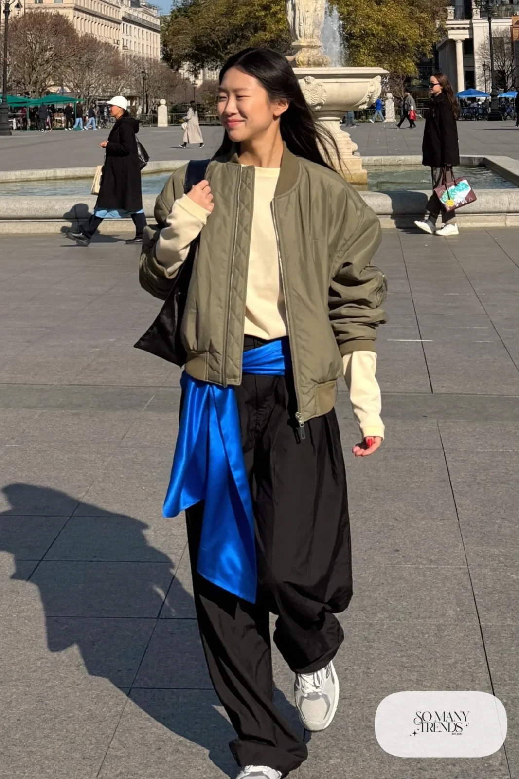 Woman in cream tee with cobalt satin sash, wide pleated black trousers, lightweight jacket and gray New Balance 9060 sneakers, outfit 6
