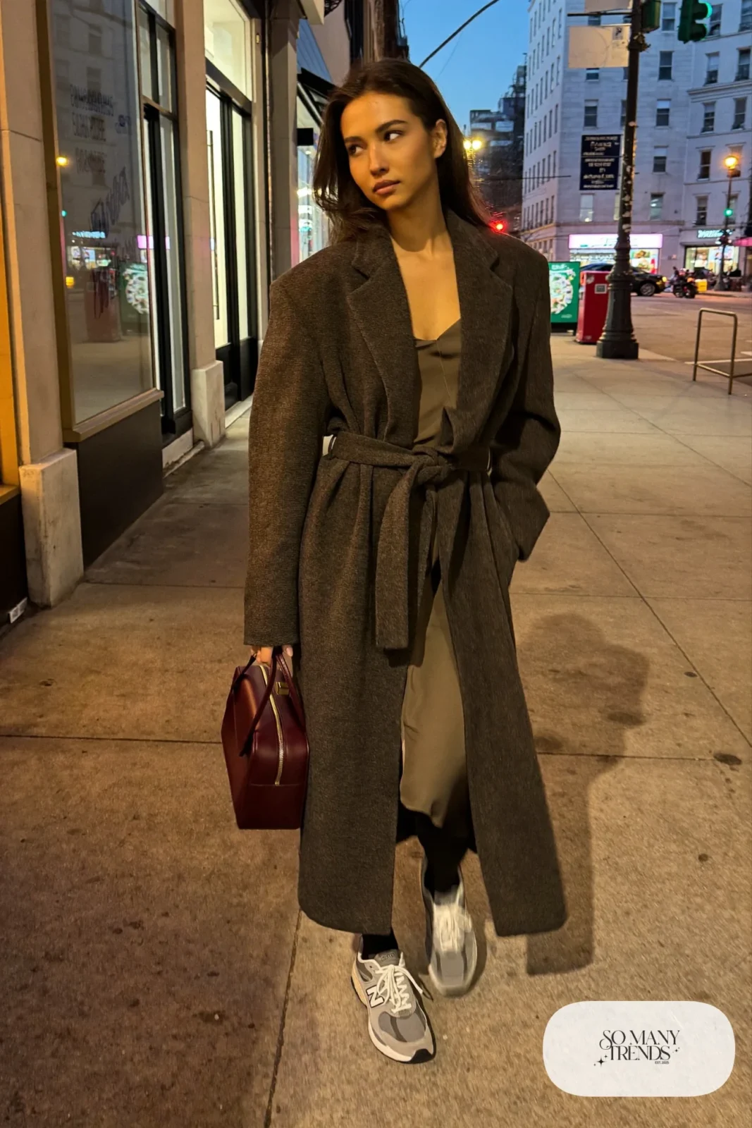 Woman in olive satin slip dress, long gray belted coat, black tights and gray New Balance 9060 sneakers, outfit 14