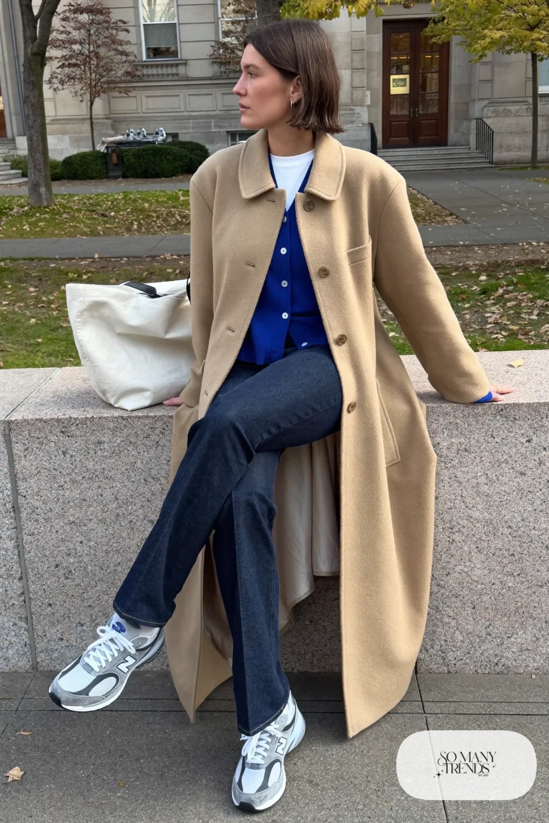 Woman in long camel coat, cobalt cardigan, white tee, dark straight jeans and gray New Balance 9060 sneakers, outfit 17