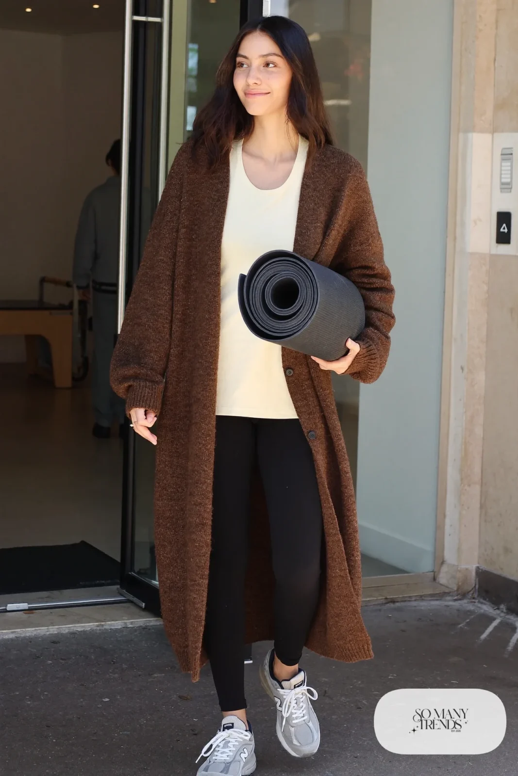 Woman in long brown cardigan coat, cream tee, black leggings and gray New Balance 9060 sneakers, outfit 27