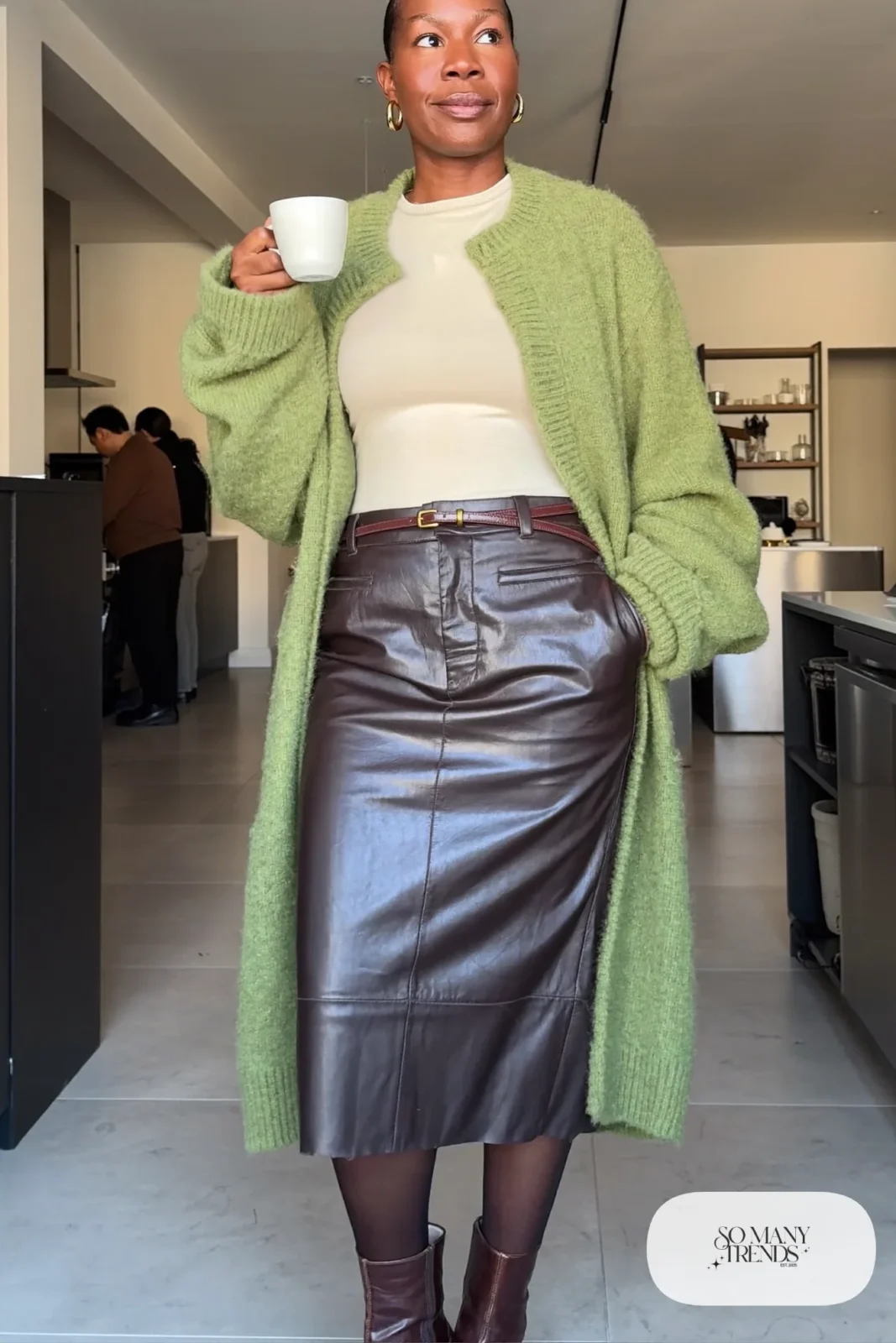 Woman in sage chunky cardigan, espresso leather midi skirt, belt and low brown boots, outfit 3