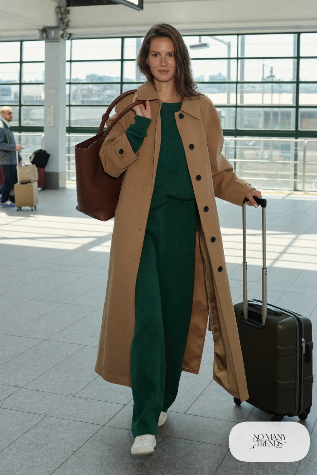 Woman in tan trench, forest green knit top and pants set, white sneakers and brown tote, outfit 8