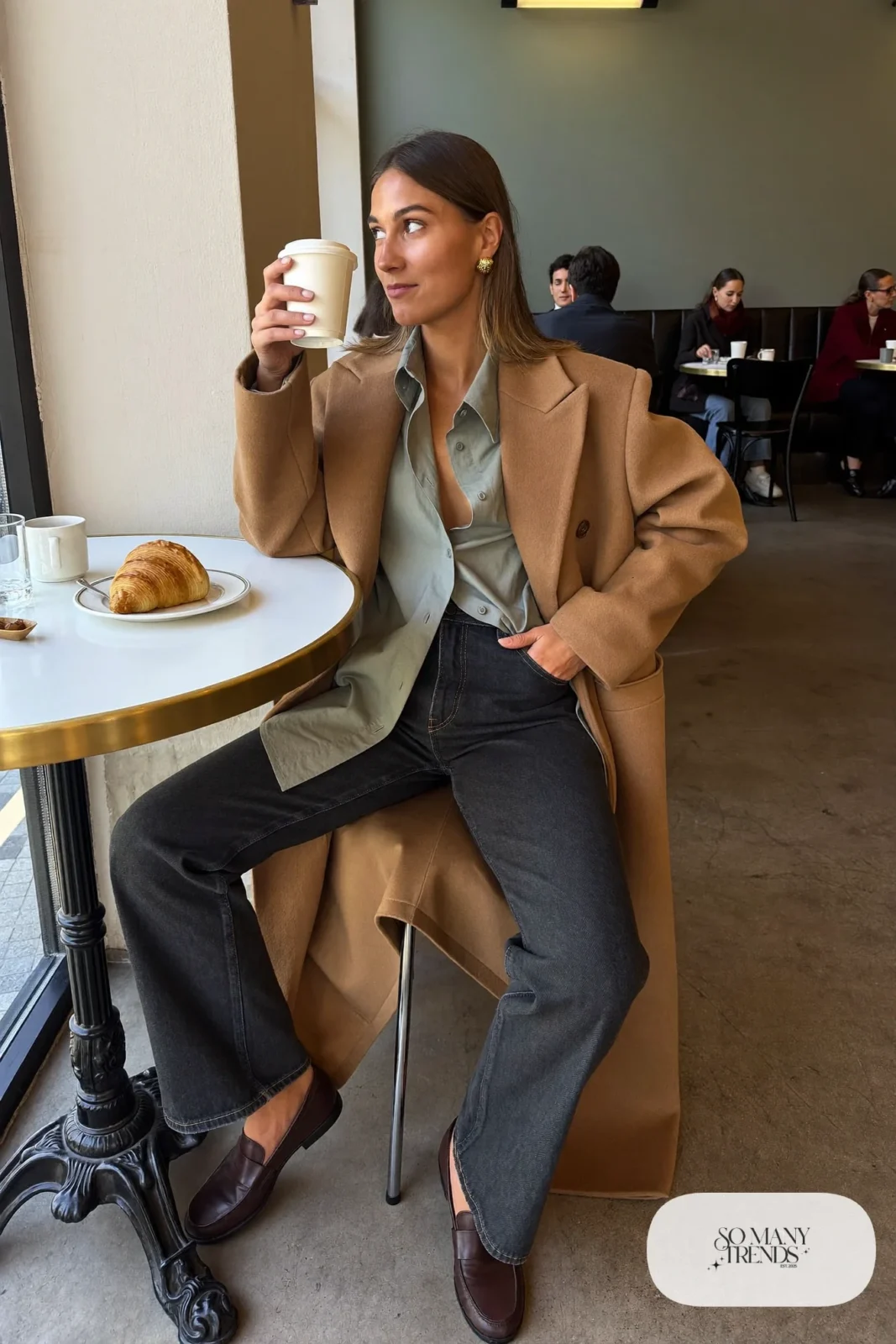 Woman in camel coat, sage button-up shirt, dark straight jeans and brown loafers, outfit 11