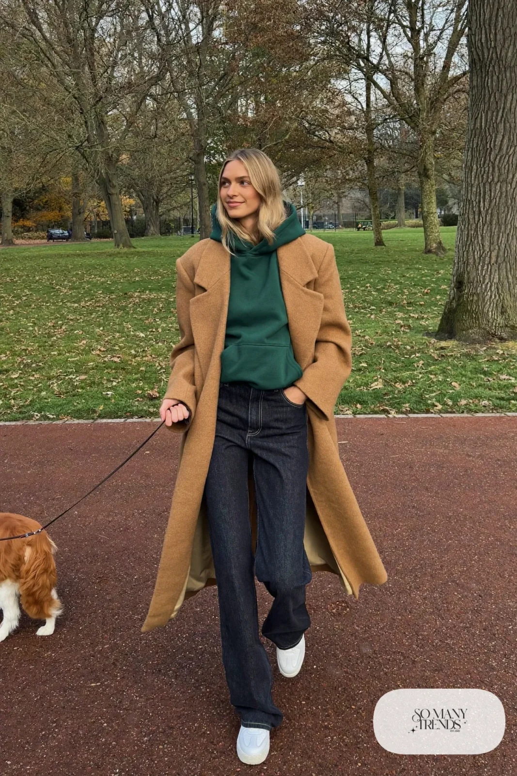 Woman in camel wool coat, forest green hoodie, dark jeans and white sneakers, outfit 32