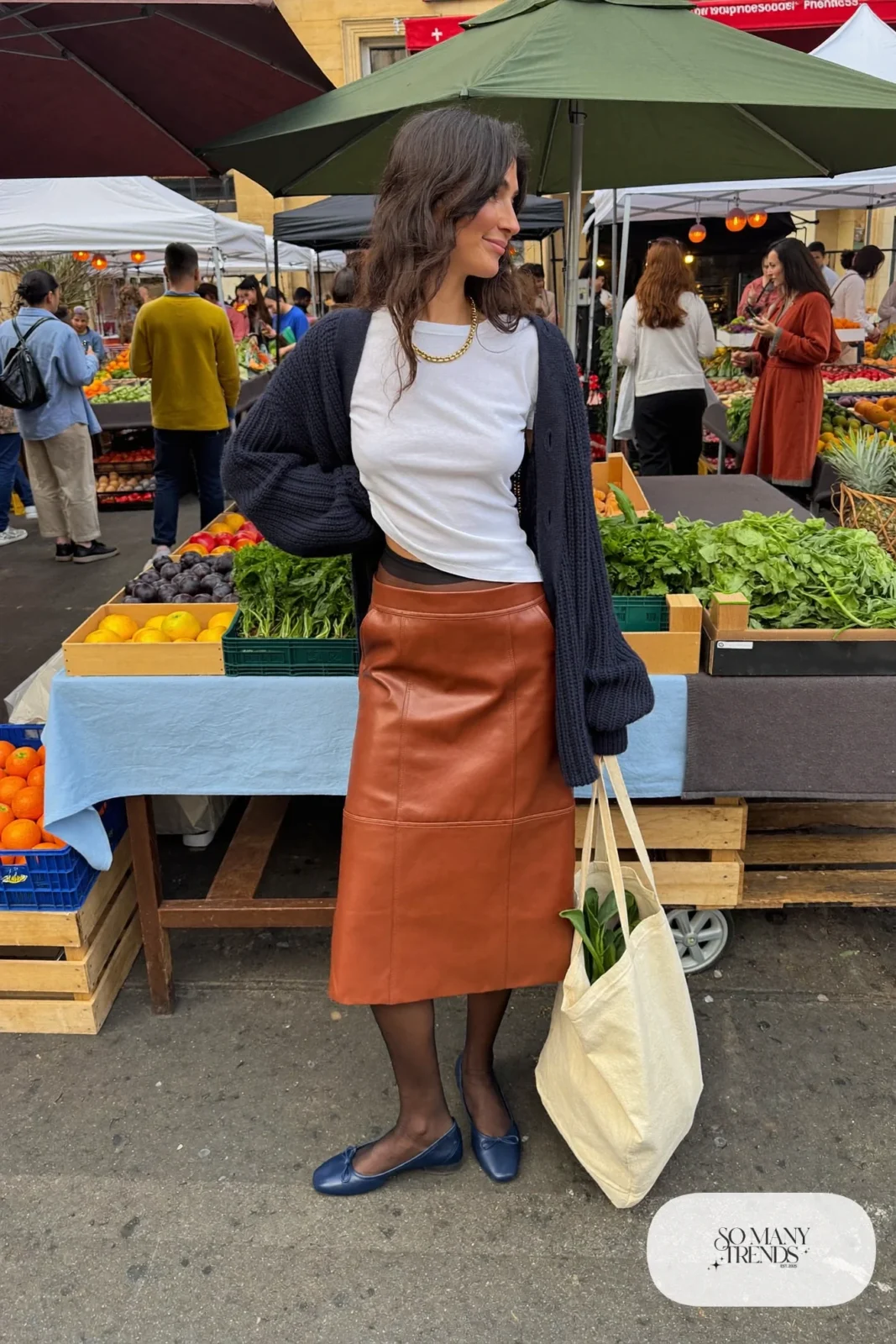 Woman in a navy cardigan, white tee, cognac leather midi skirt and navy ballet flats, outfit 3