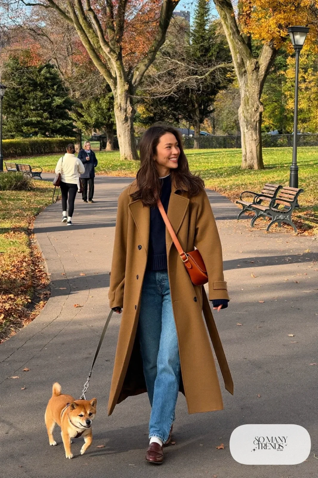 Woman in a camel trench coat, navy sweater, straight blue jeans and brown loafers, outfit 6