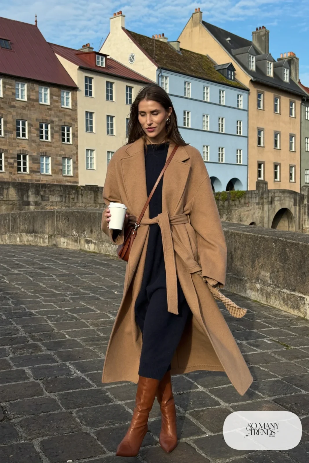 Woman in a camel wrap coat, navy sweater midi dress, sheer tights and cognac tall boots, outfit 13