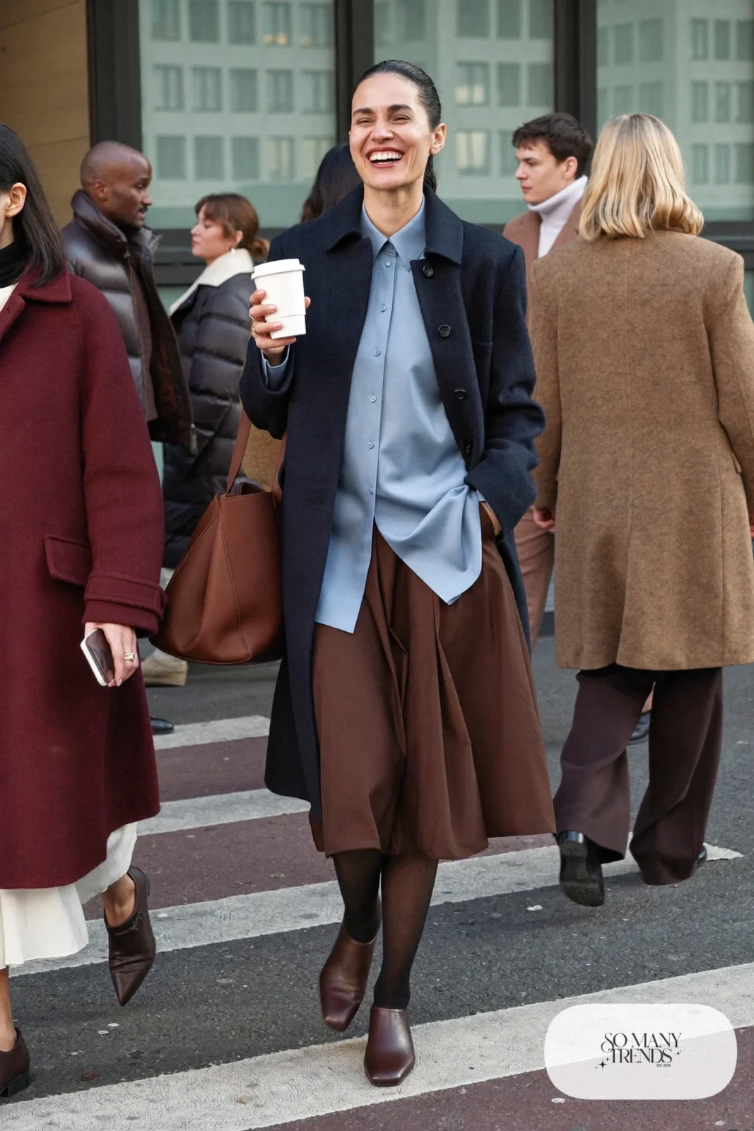 Woman in a long navy coat, powder blue shirt, chocolate pleated midi skirt and brown flat boots, outfit 15
