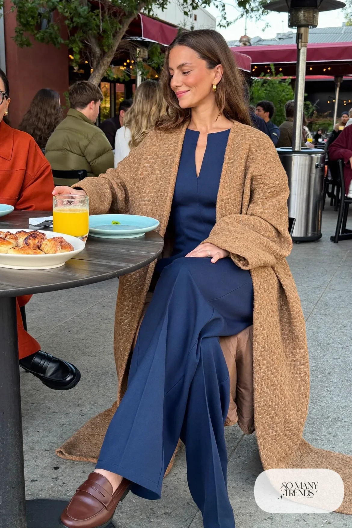 Woman in a navy wide-leg jumpsuit, long camel cardigan coat and brown loafers, outfit 16