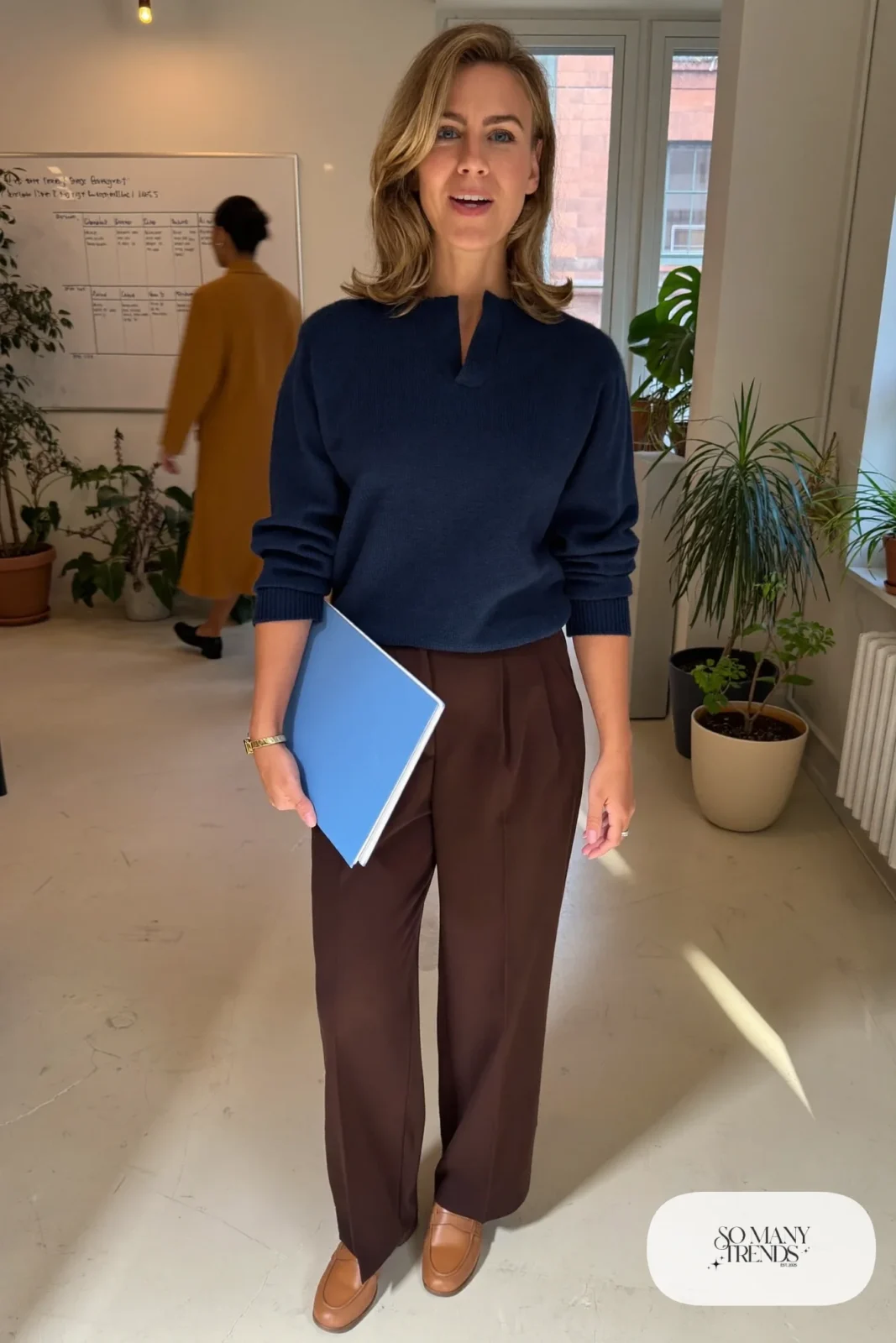 Woman in a navy sweater, chocolate pleated trousers and camel loafers, outfit 19