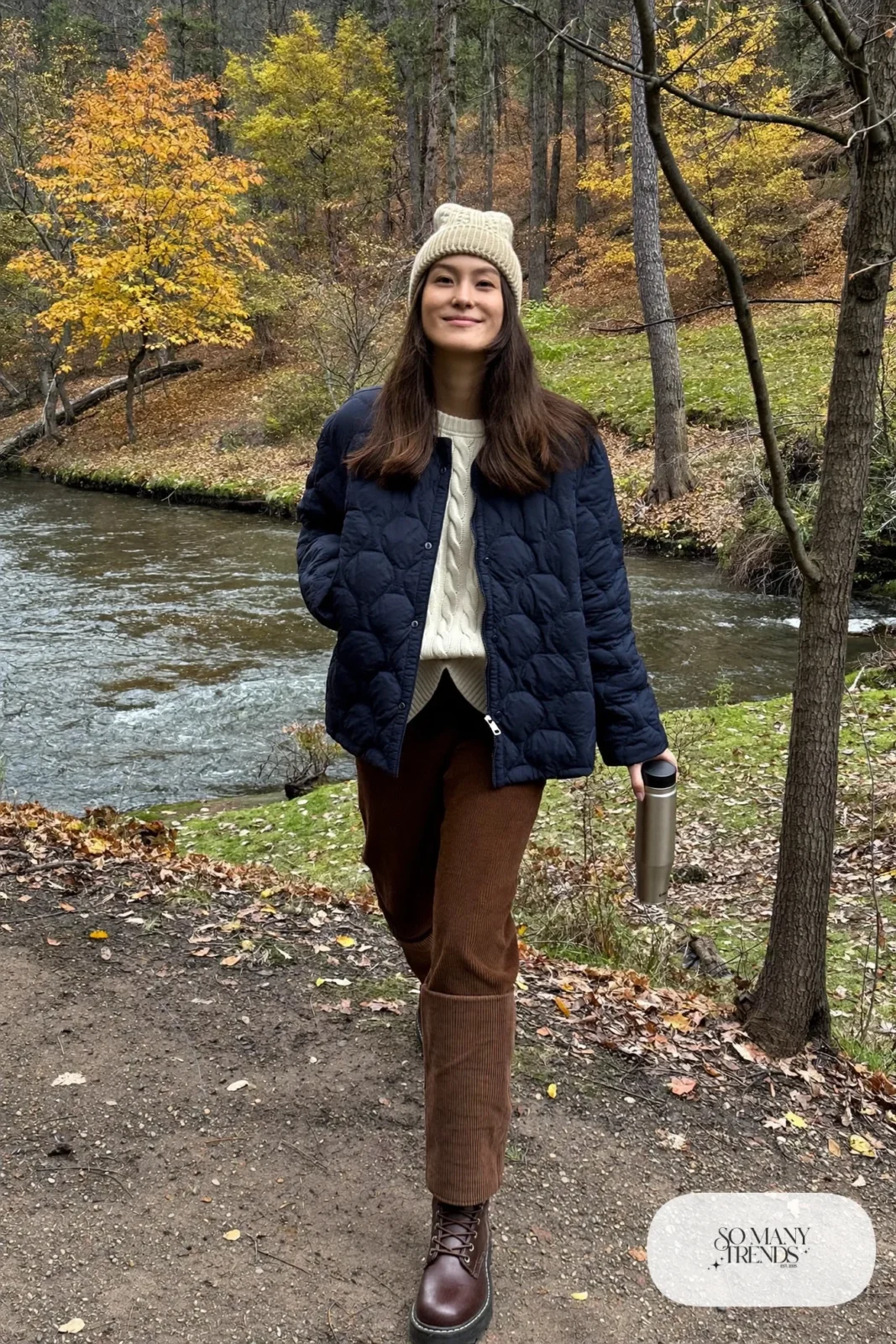 Woman in a navy quilted jacket, cream knit sweater, brown corduroy pants and brown lace-up boots, outfit 24