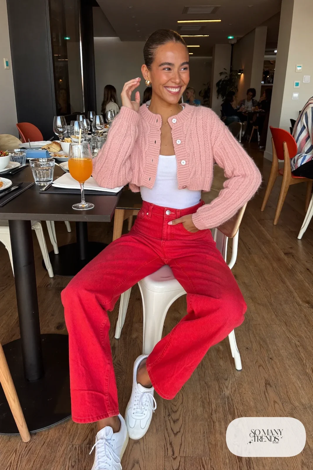 Woman in a cropped blush pink cable-knit cardigan, white tank, red straight-leg jeans and white sneakers, outfit 3