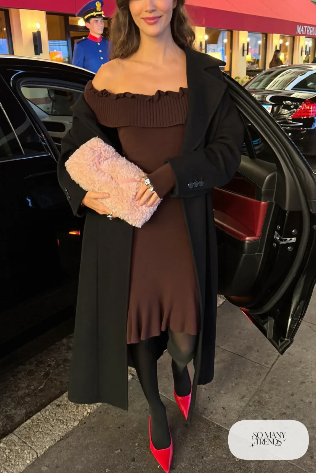 Woman in a chocolate brown off-the-shoulder knit dress with a pink shearling clutch, red pumps and a long black coat, outfit 11
