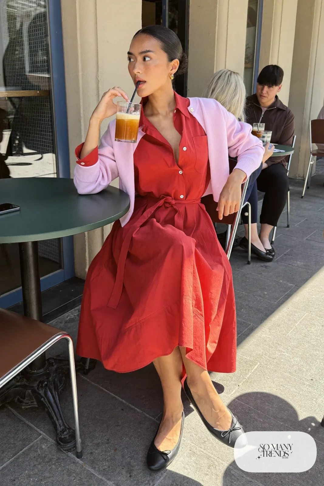 Woman in a red poplin shirtdress with a belted waist, pink cardigan worn over the arms and black ballet flats, outfit 27