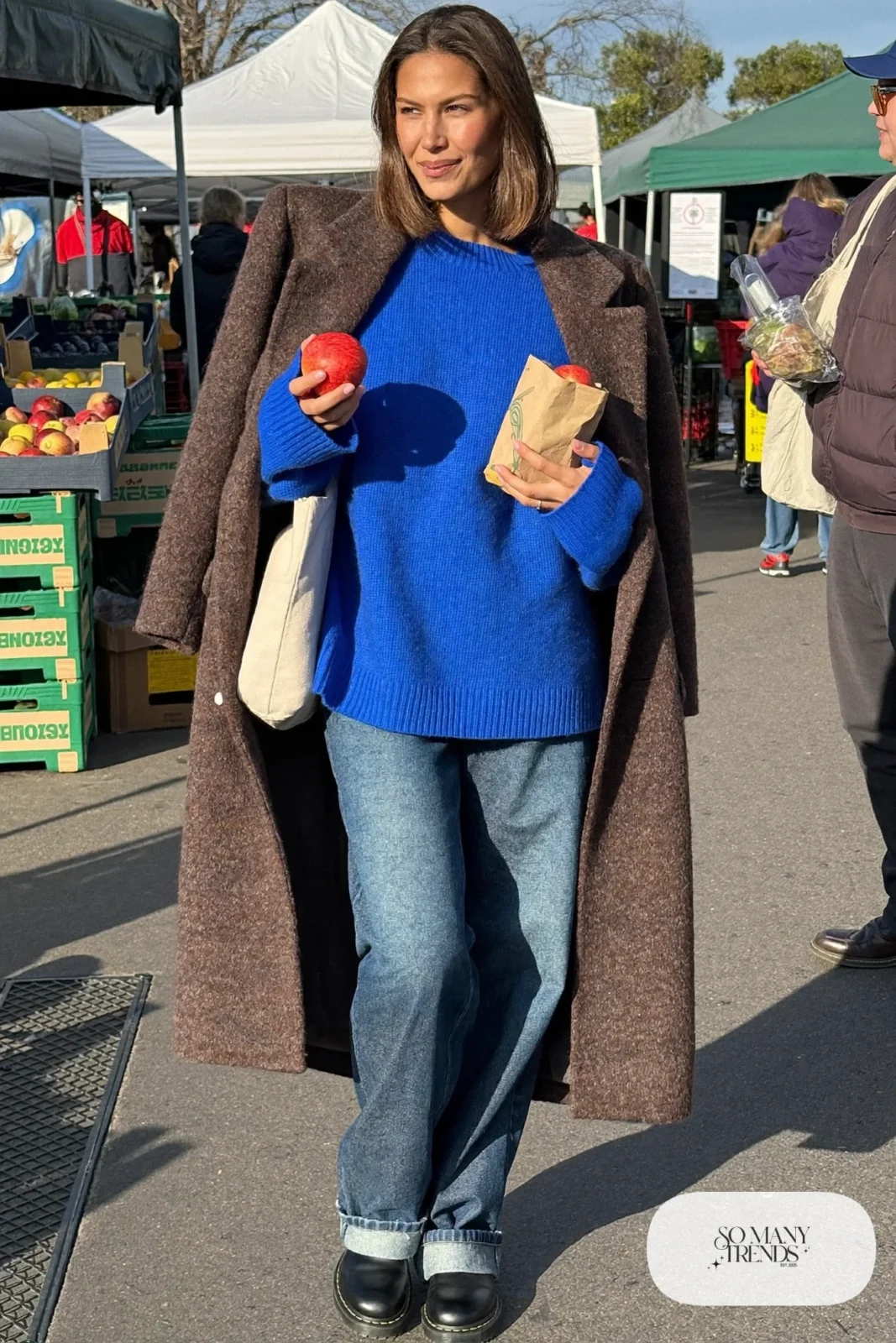 Woman in a long gray cocoon coat, cobalt blue chunky sweater, wide-leg indigo jeans and black lug-sole boots, outfit 3