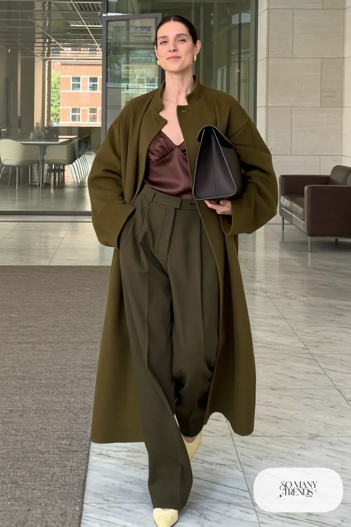 Woman in a long olive wool cocoon coat, brown satin cami, dark olive pleated wide pants and cream flats, outfit 4