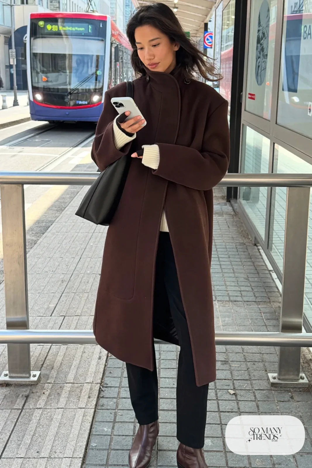 Woman in a chocolate brown funnel neck wool coat, cream knit top, straight black pants and brown ankle boots, outfit 6