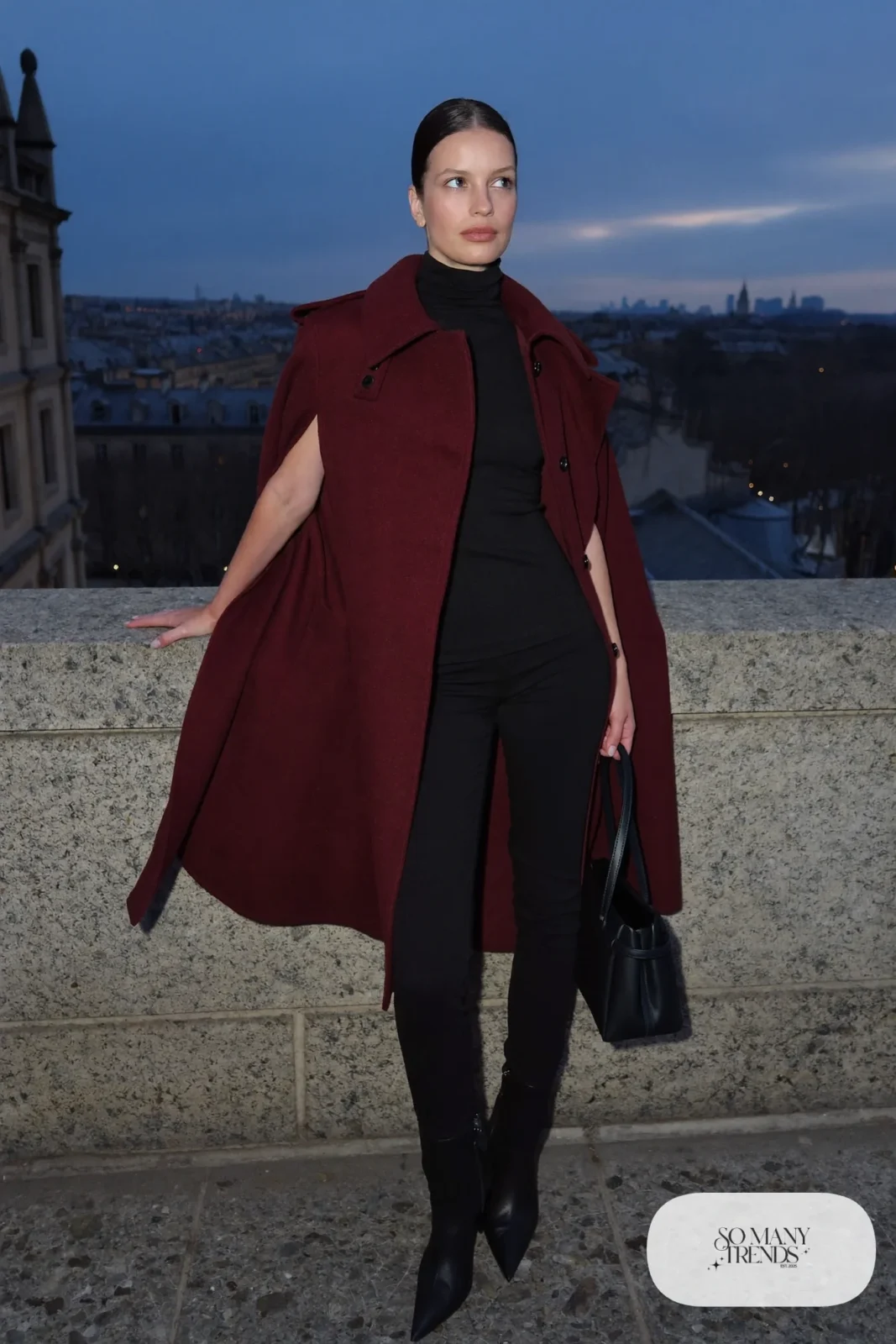 Woman in a wine wool cape coat, black fitted turtleneck, slim black pants and black pointed ankle boots, outfit 8