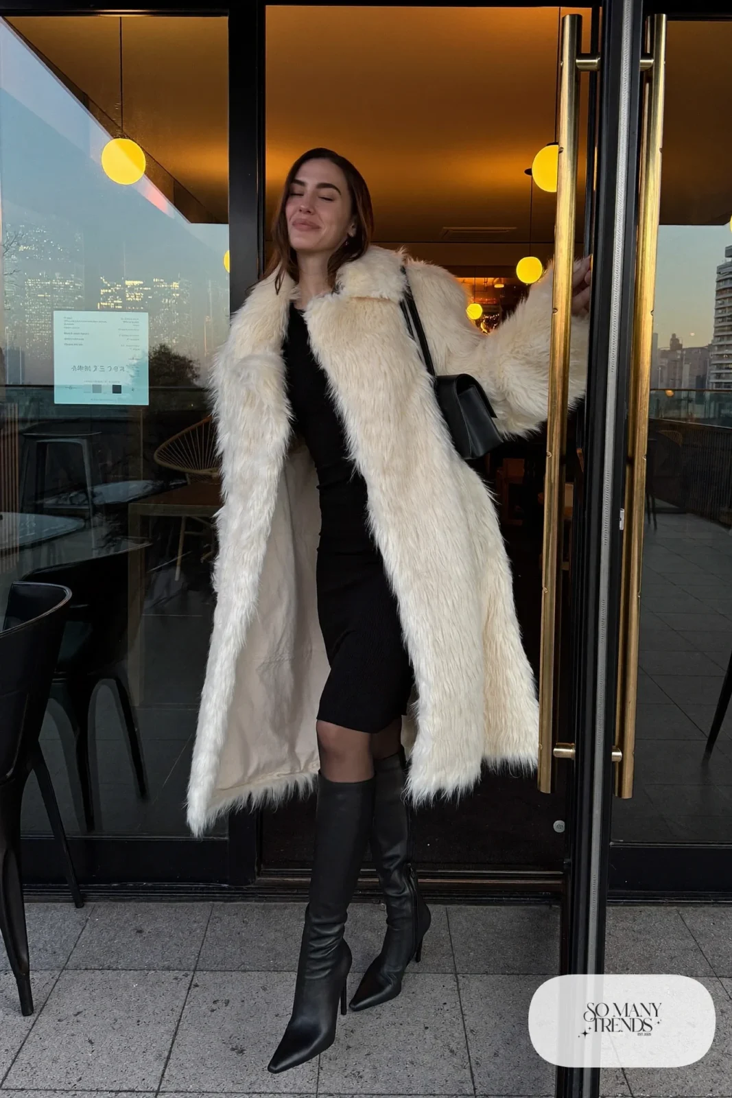 Woman in an ivory faux fur coat over a black knit midi dress, sheer black tights and black knee-high boots, outfit 11