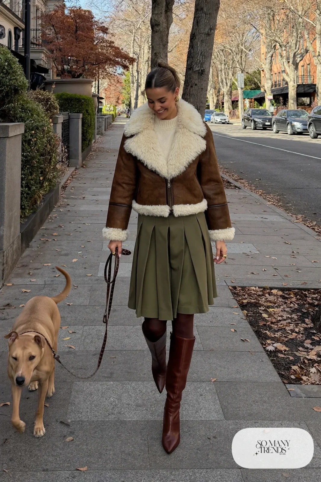 Woman in a brown shearling aviator jacket, cream knit sweater, olive pleated midi skirt and tall brown boots, outfit 13