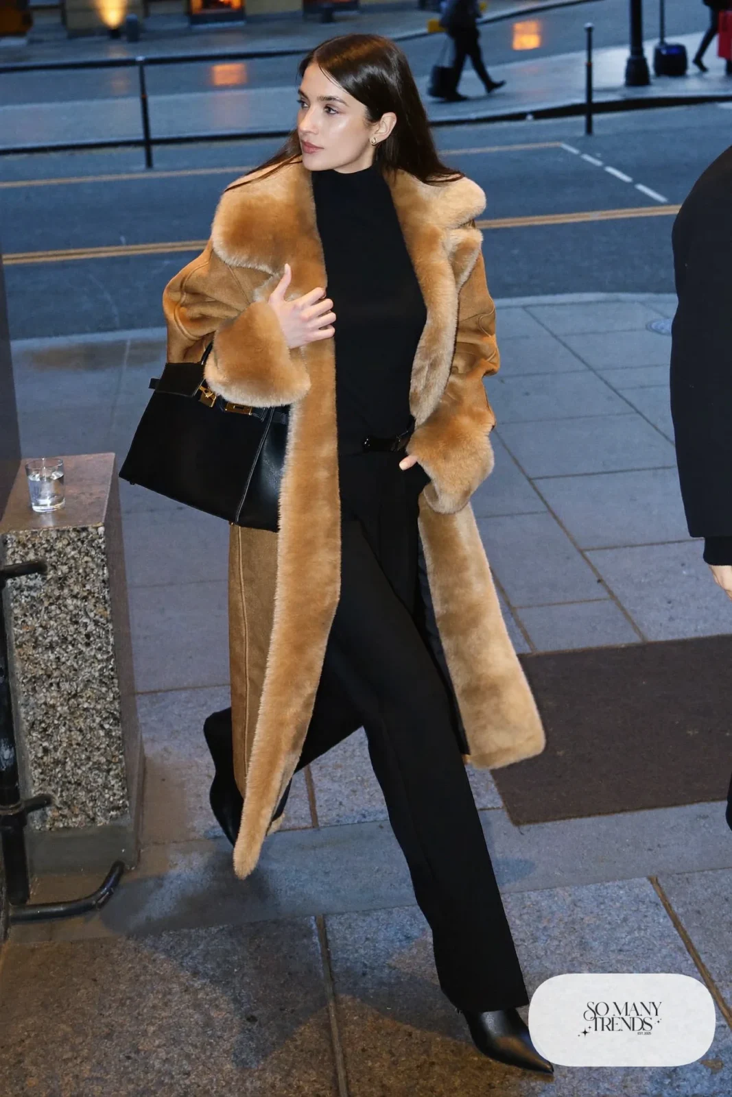 Woman in a long tan shearling coat, black turtleneck, straight black wool pants and black pointed boots, outfit 14