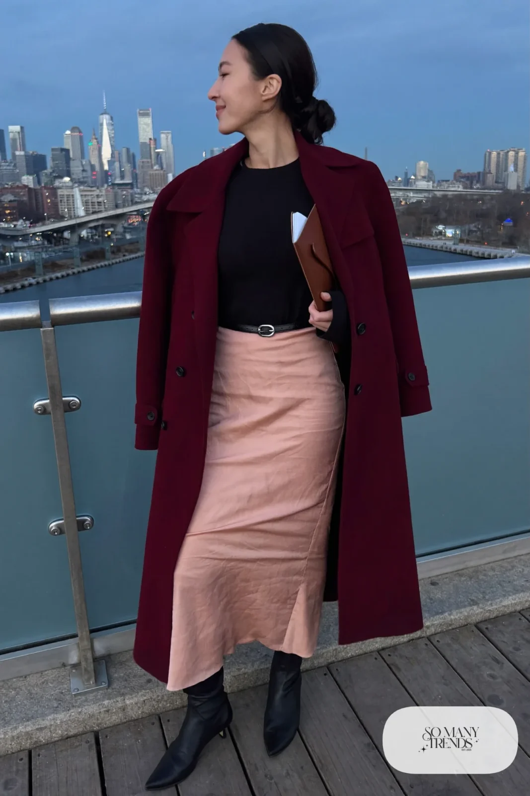 Woman in a burgundy wool coat over a blush satin midi skirt, black fitted knit, black tights and black boots, outfit 18