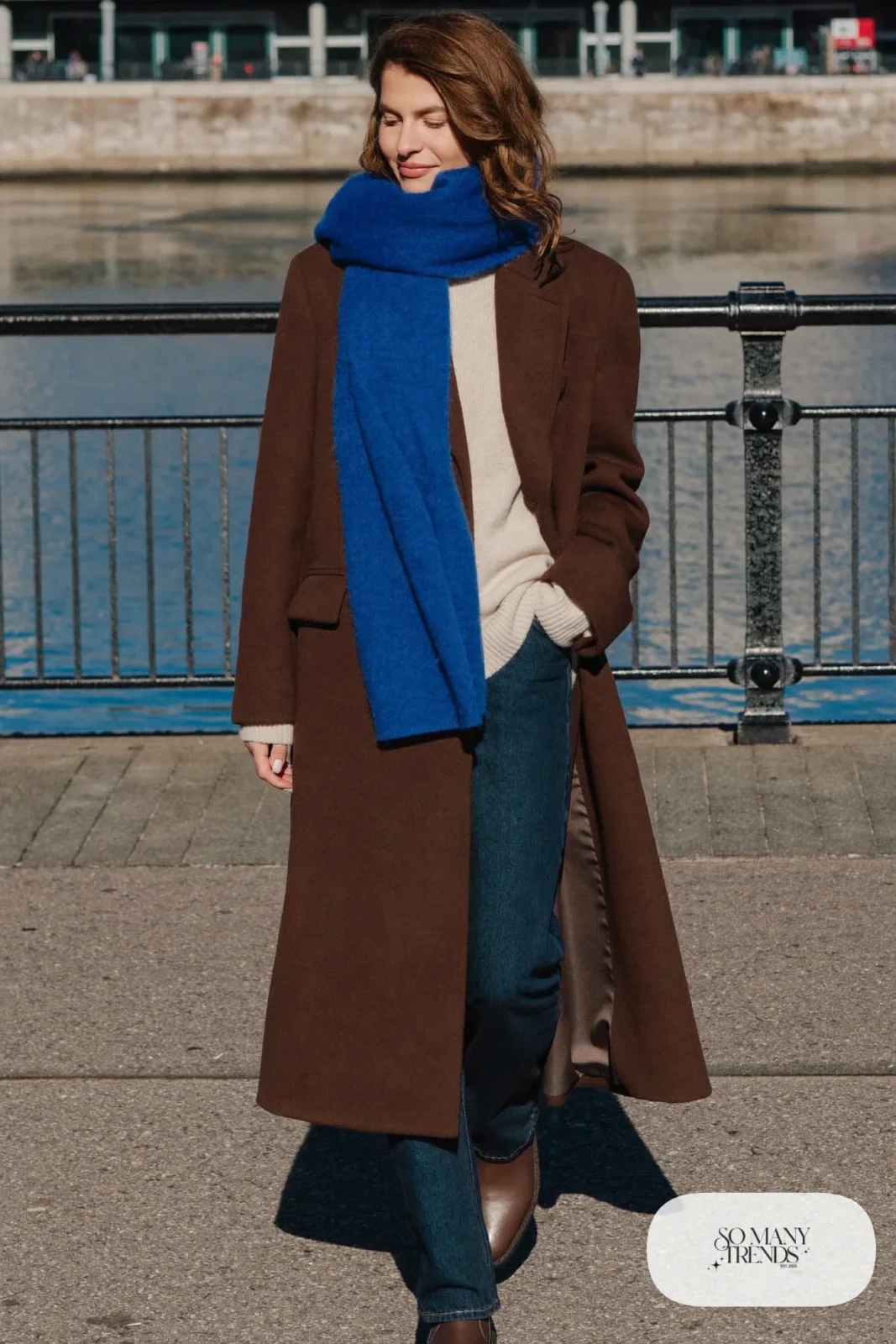 Woman in a chocolate wool coat, cobalt blue scarf, cream knit, dark straight jeans and brown boots, outfit 22