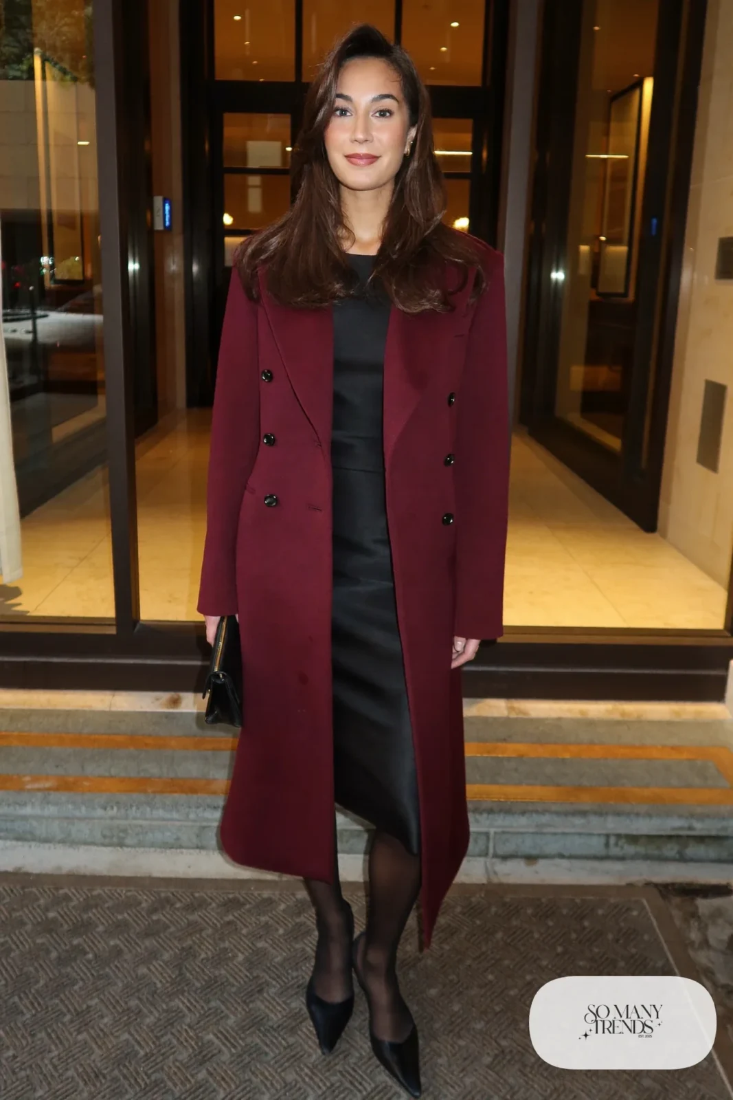 Woman in a wine double-breasted tailored wool coat over a black column dress with black pointed pumps, outfit 28