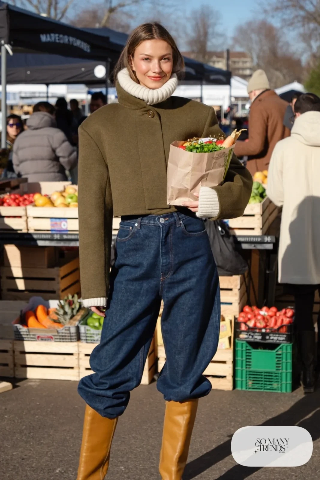 Woman in cropped olive jacket, white ribbed turtleneck, dark wide-leg jeans and tan knee boots, outfit 6