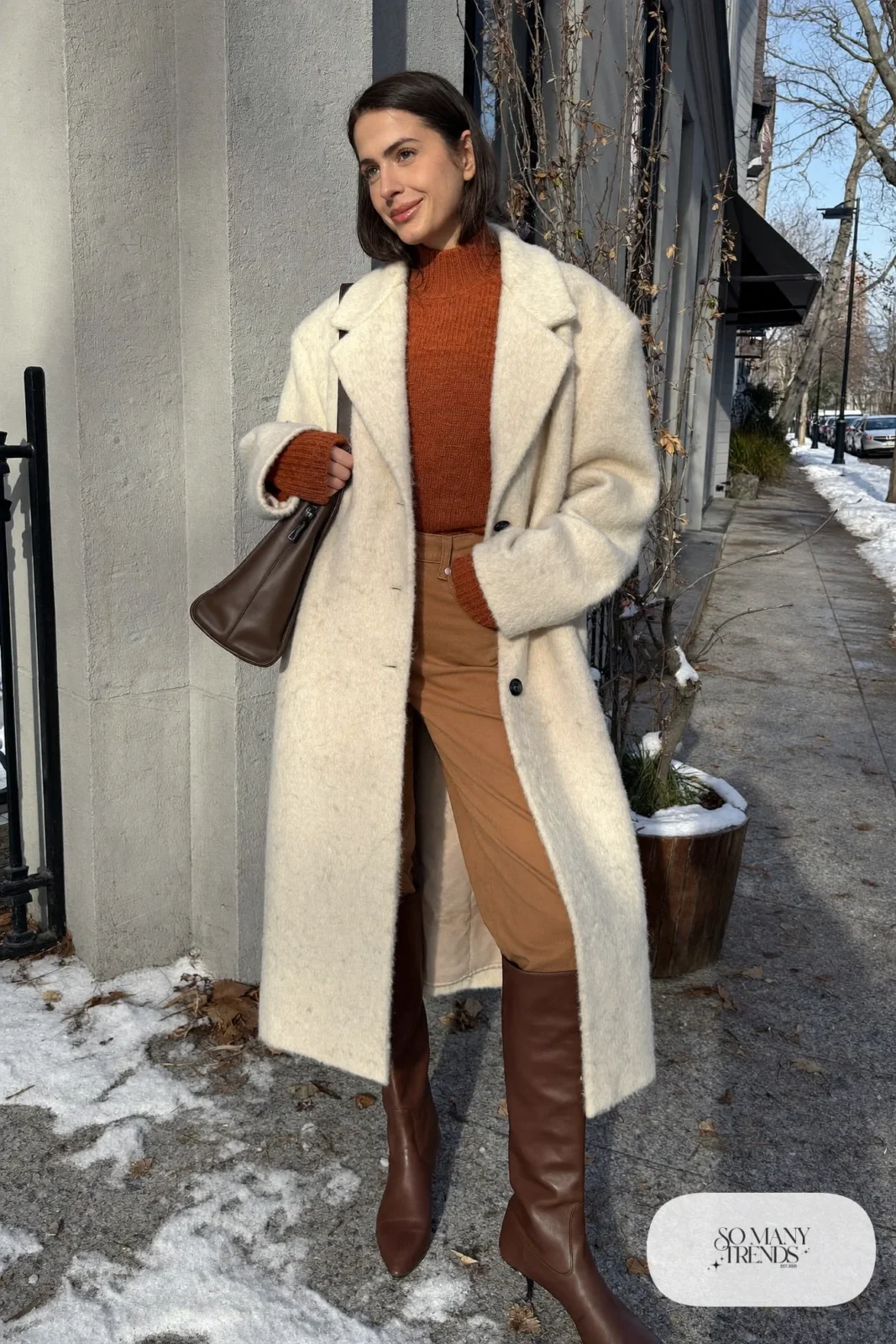 Woman in long cream wool coat, rust knit, camel pants and chocolate leather boots, outfit 13