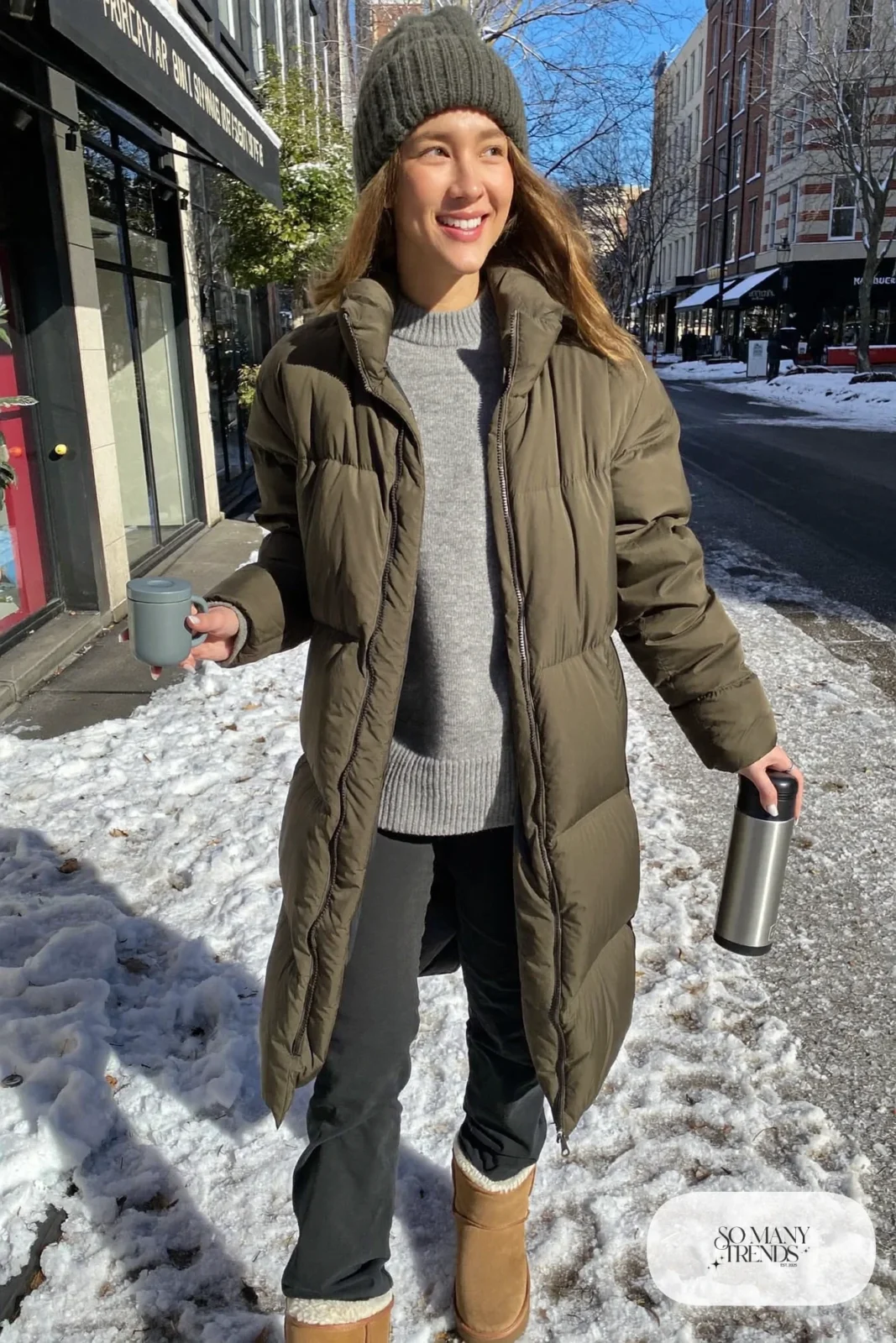 Woman in long olive puffer coat, gray sweater, black pants and shearling-lined tan boots, outfit 26