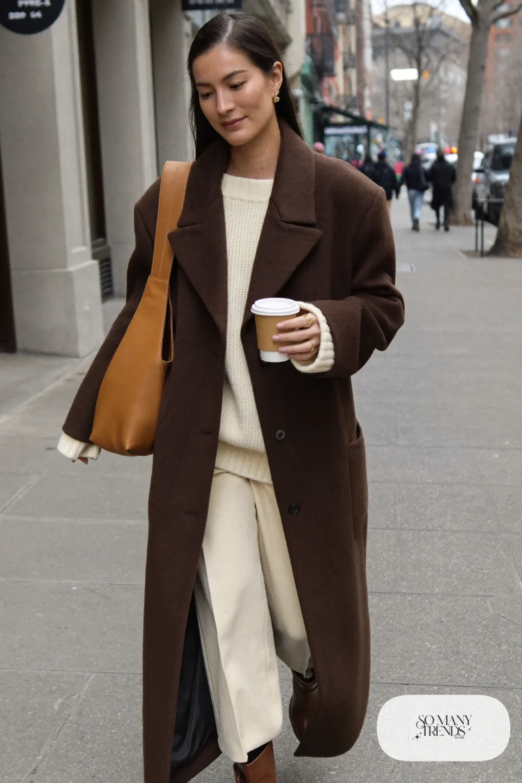 Woman in long chocolate brown wool coat over cream knit sweater, cream straight pants and brown leather boots, outfit 1