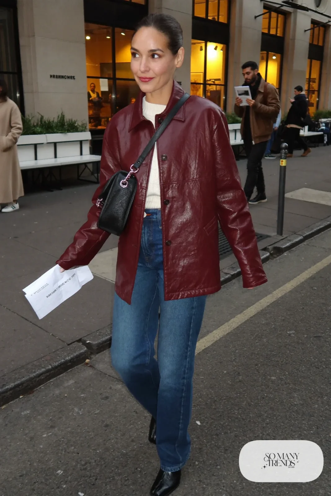 Woman in oxblood boxy leather jacket, cream sweater, dark blue straight jeans and black ankle boots, outfit 7