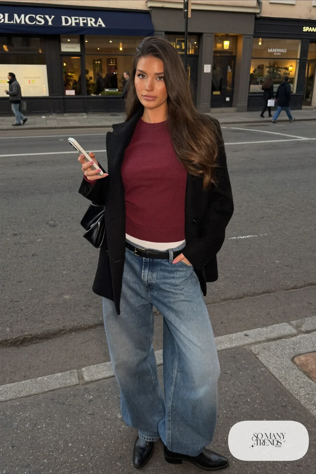 Woman in baggy light-wash jeans, fitted burgundy knit, black belt and black leather boots, look 6