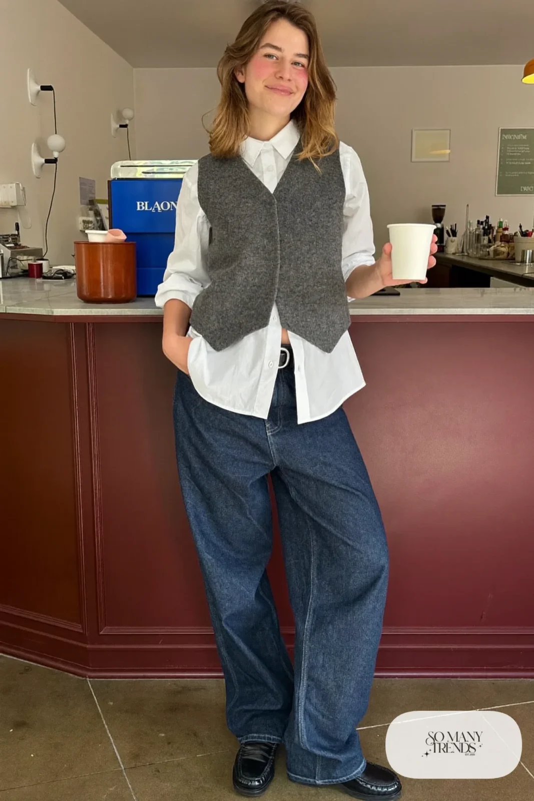 Woman in baggy dark jeans, gray knit vest over a white shirt and black loafers, look 10
