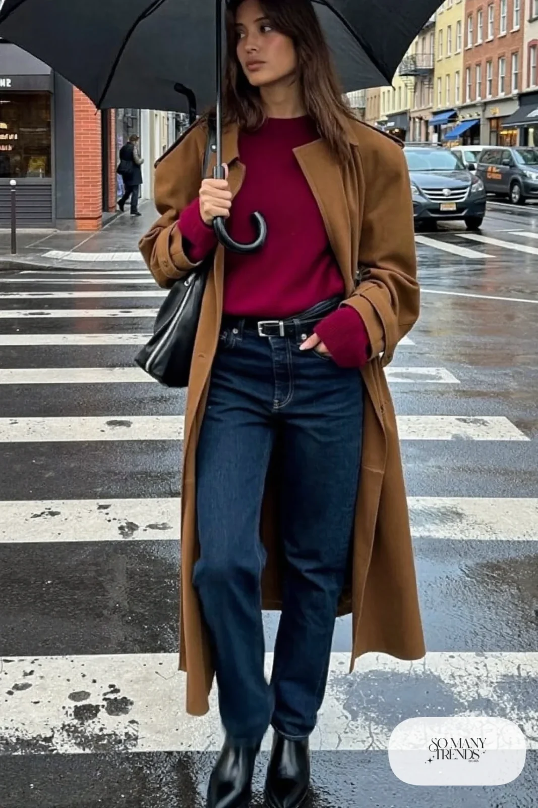 Woman in dark indigo jeans, camel trench coat, burgundy sweater and black ankle boots, look 11