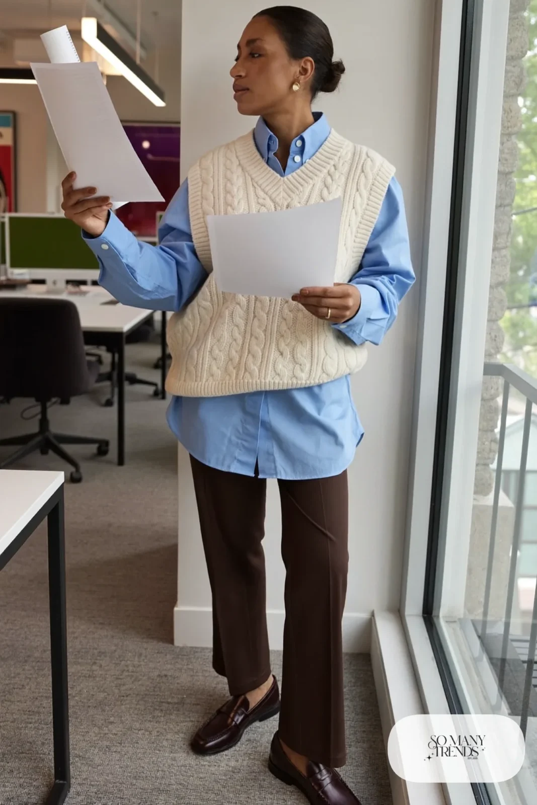 Woman in a cream cable knit vest over a sky blue shirt, chocolate brown pants and loafers, outfit 10