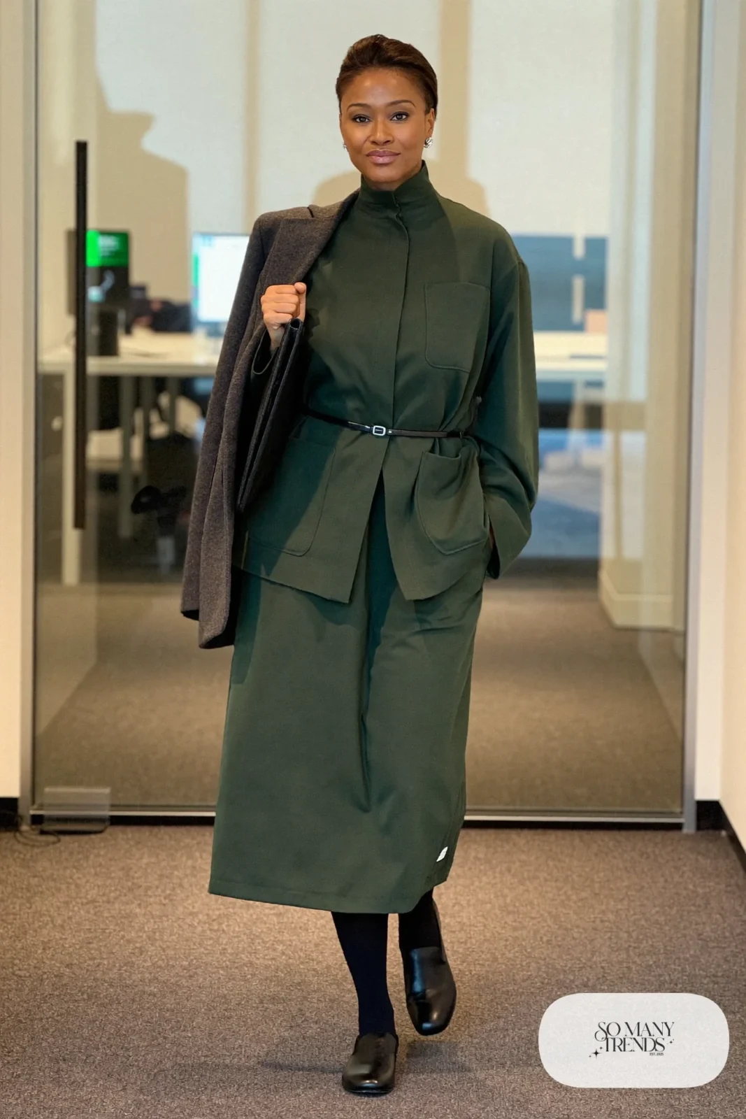 Woman in a forest green midi dress with a charcoal belted blazer, black tights and loafers, outfit 17