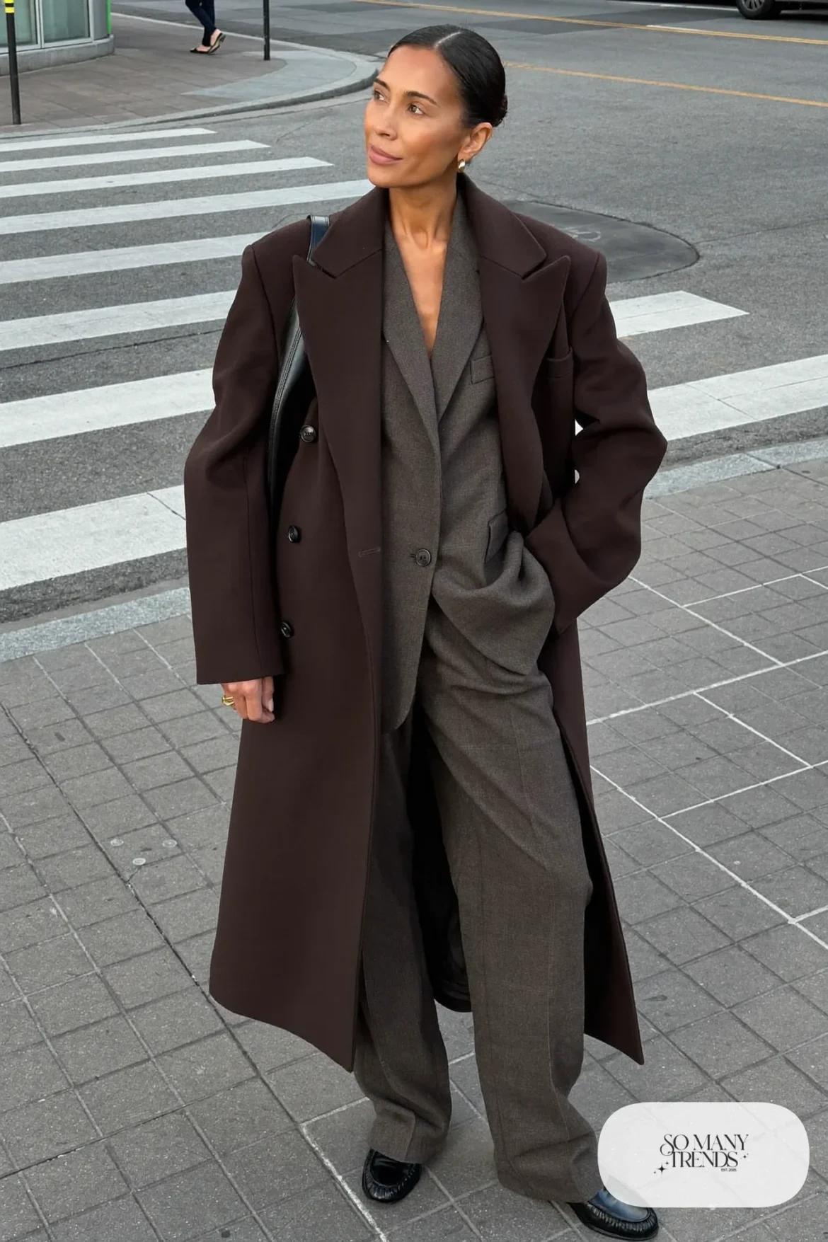Woman in a chocolate brown wool overcoat over a gray flannel suit with black loafers and a bag, outfit 21