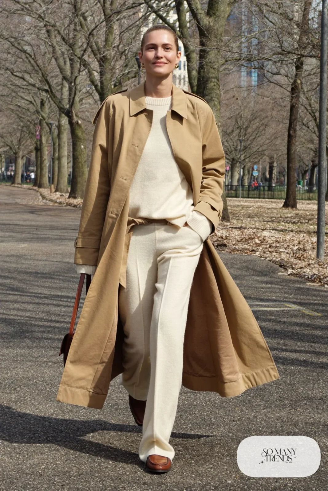 Woman in a camel trench coat over a cream knit sweater and pants with brown loafers, outfit 24