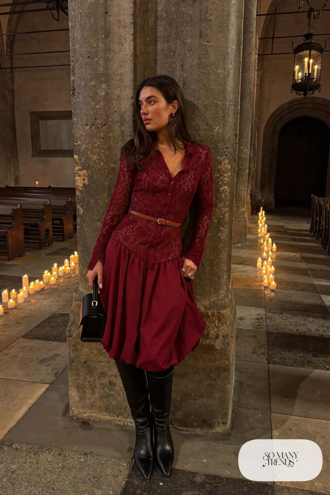 Woman in a burgundy long-sleeve lace midi dress, cognac leather belt, black tights and tall black boots, outfit 3
