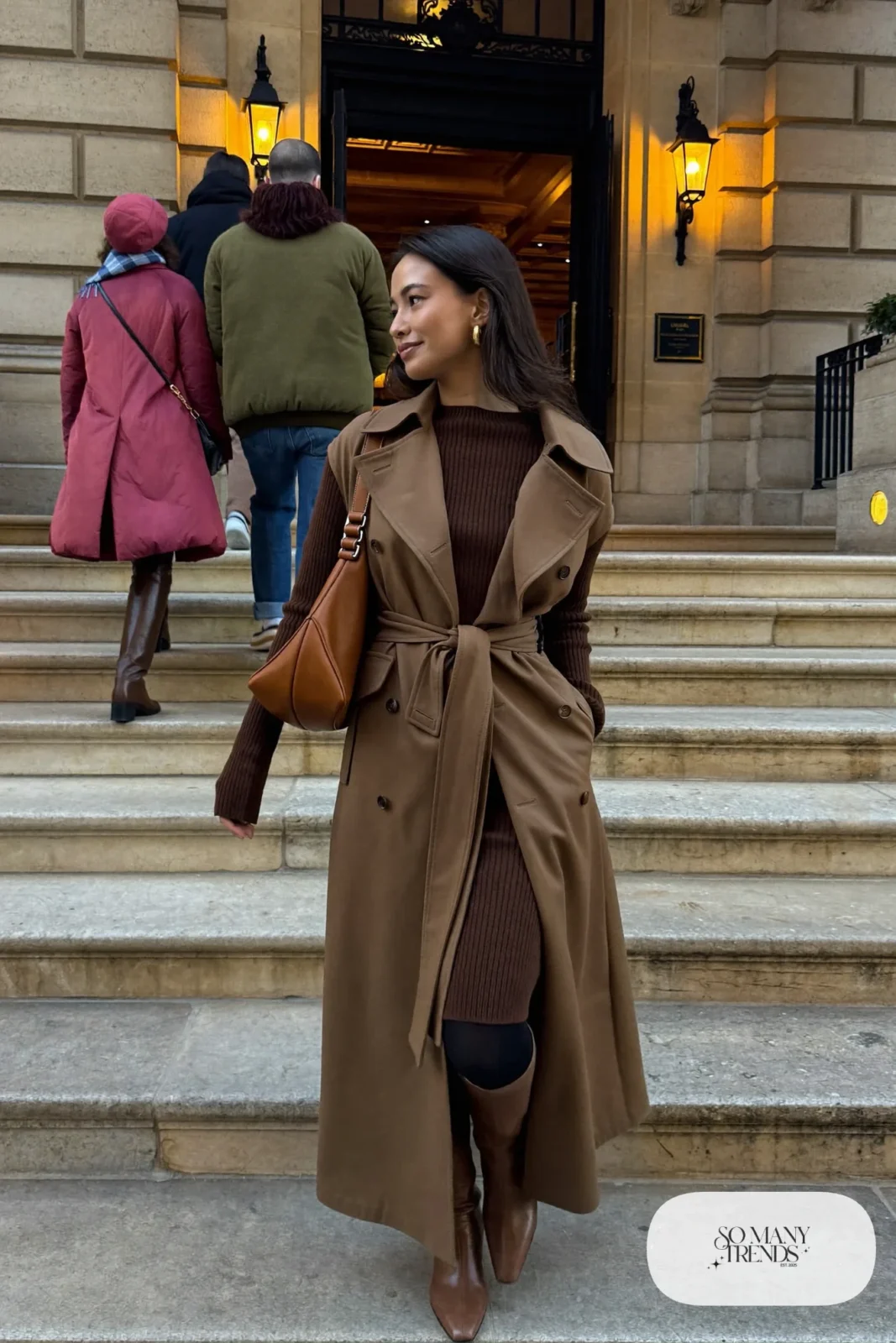 Woman in a chocolate brown ribbed knit midi dress, camel belted trench coat, cognac bag and brown tall boots, outfit 4