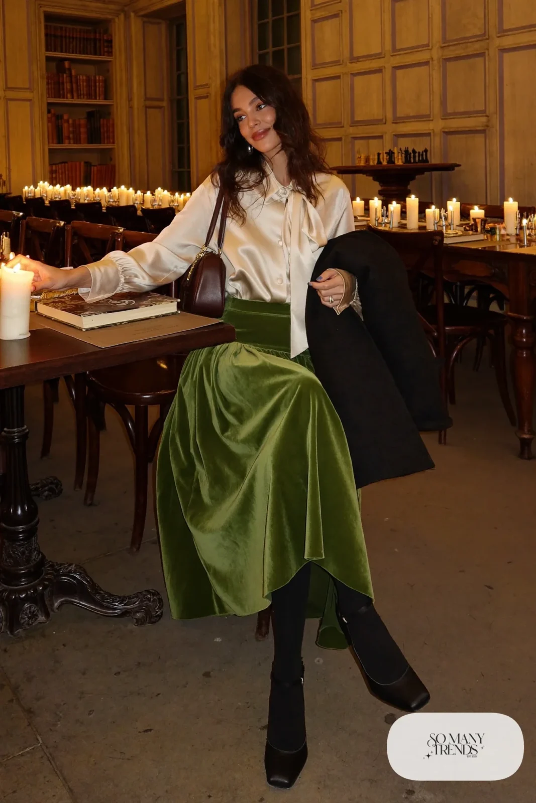 Woman in a moss green velvet midi skirt, cream satin blouse with a bow collar, black sheer tights and black pumps, outfit 7