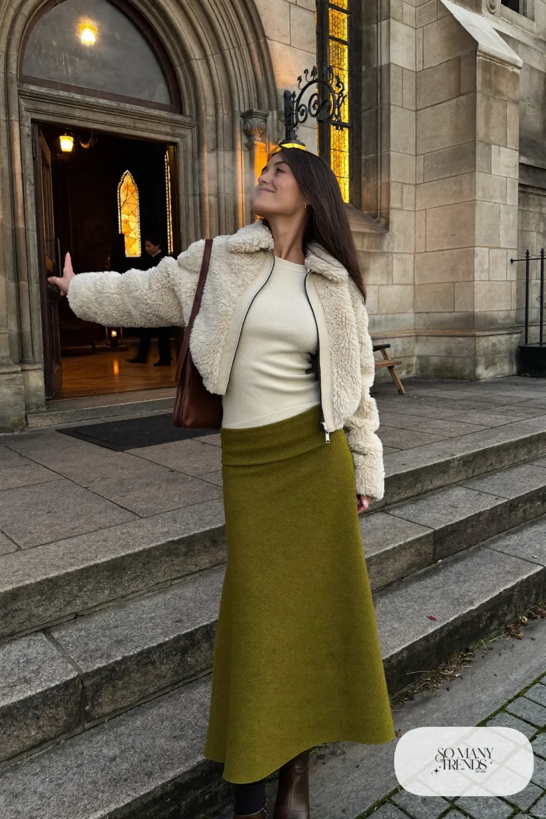 Woman in a moss green wool maxi skirt, cream cropped shearling jacket, fitted cream knit top and brown boots, outfit 12
